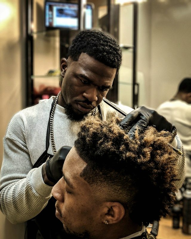 A barber shaping a client's textured crop with clippers.