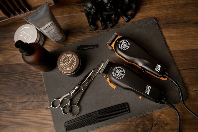 Clippers, shears, a comb and pomade laid out on a slate board.