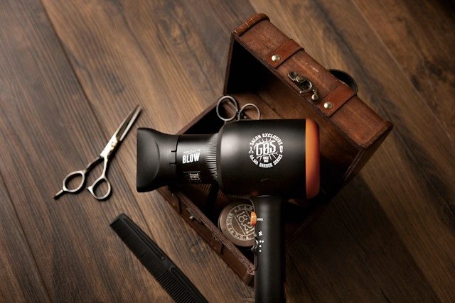 Shears, a dryer and pomade arranged on a dark wooden counter.