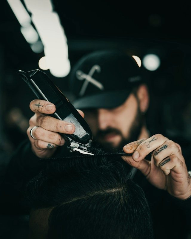 A barber checking a clipper guard under the shop lights.