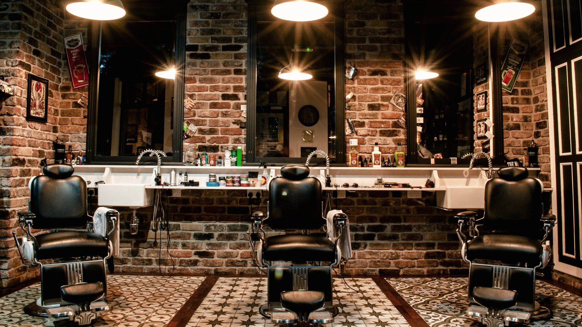 The floor at Kenny's Barbering Co. — four vintage barber chairs beneath brass pendant lights against an exposed brick wall.